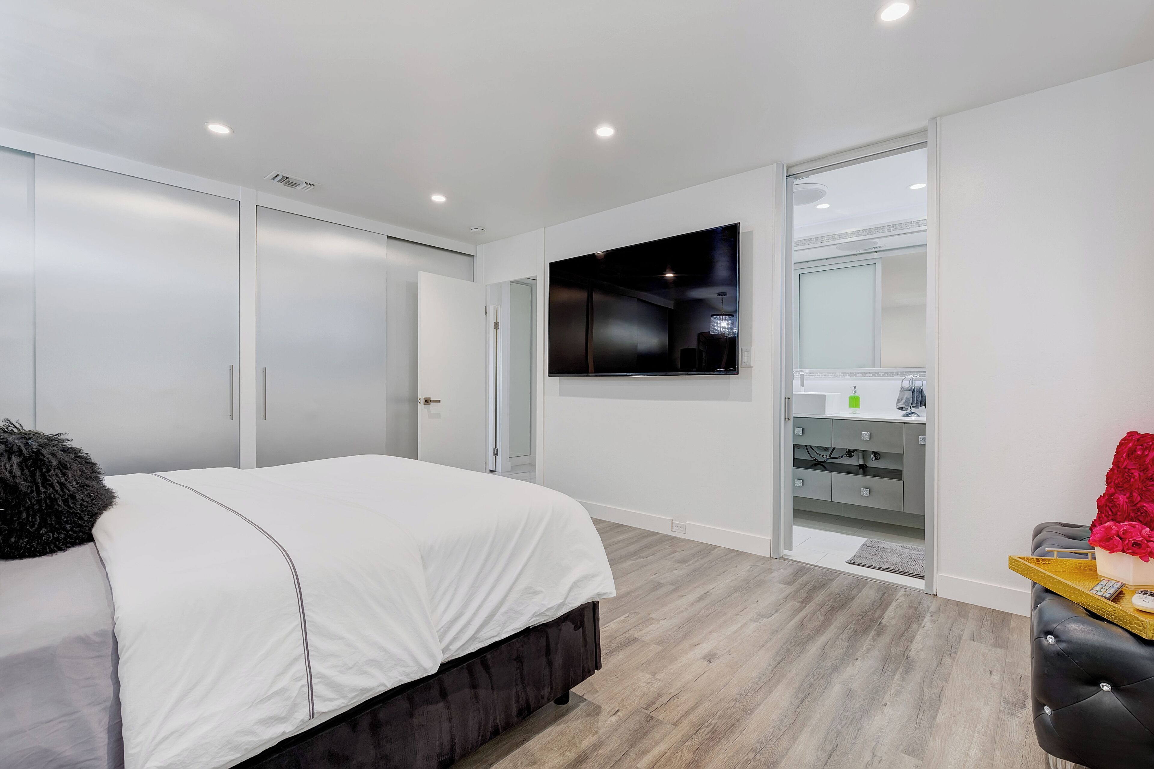 A modern bedroom with a bed, a TV, a vanity, and a walk-in closet.