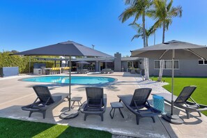 A backyard with a swimming pool, lounge chairs, umbrellas, and a well-maintained lawn.