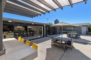Uma área de pátio externa com espaço coberto para sentar, piscina e espaço para refeições.