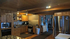 A modern kitchen with wooden cabinets, stainless steel appliances, and a granite countertop. - Historic Lodge on 48 Acres Overlooking Long Lake Updated for Accessibility (Walker)