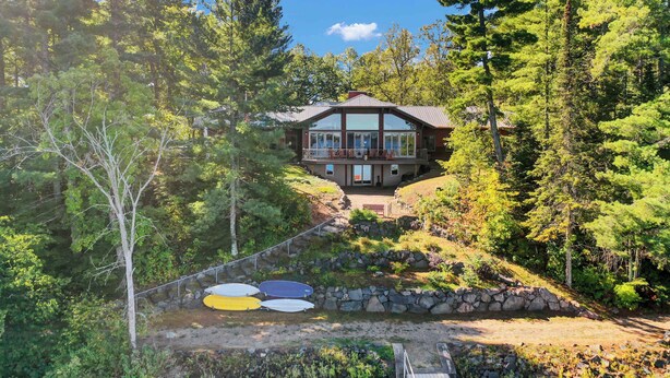 A cabin with a large glass front, surrounded by dense forest, and a stone staircase leading up to it. - Historic Lodge on 48 Acres Overlooking Long Lake Updated for Accessibility (Walker)