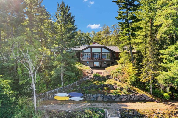 A cabin with a large glass front, surrounded by dense forest, and a stone staircase leading up to it.