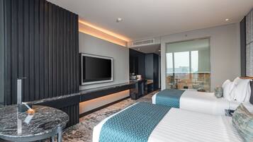 Una habitación de hotel moderna con una cama grande, un televisor montado en la pared, una mesita redonda y una zona de estar con vistas a la ciudad.
