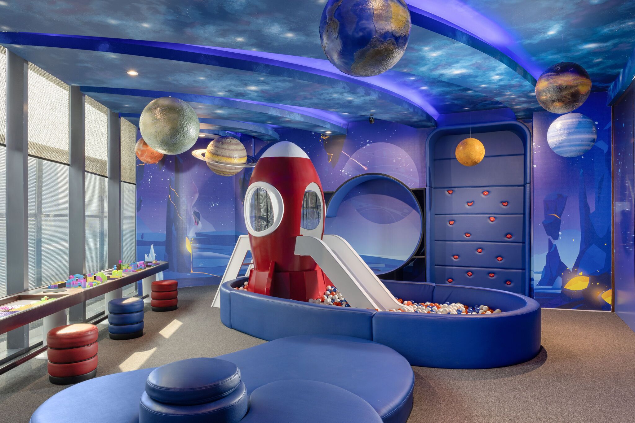 A play area with a slide, ball pit, and space-themed decorations including planets and a rocket.