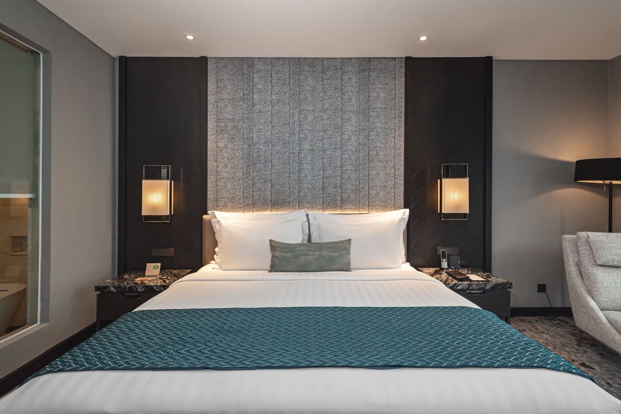A modern hotel room with a large bed, two bedside tables with lamps, a large window, and a view of the city.