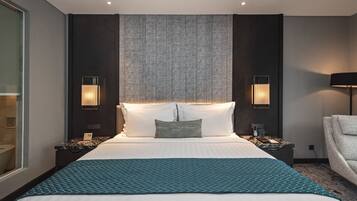 A modern hotel room with a large bed, two bedside tables with lamps, a large window, and a view of the city.