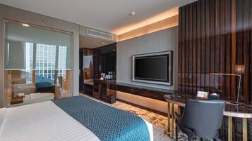 A modern hotel room with a large bed, a desk with a chair, a flat-screen TV, and a balcony with a city view.