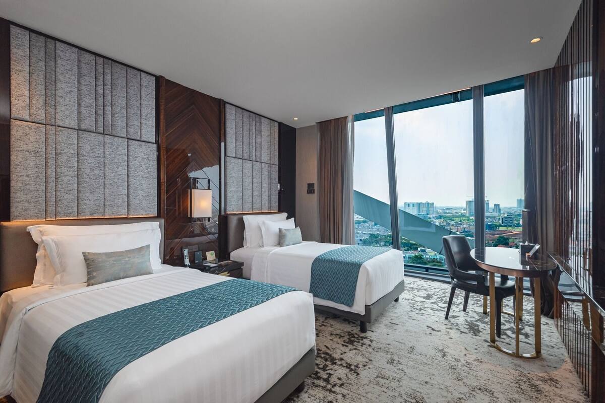 A hotel room with two beds, a view of the city, and a dining area with a table and chairs.