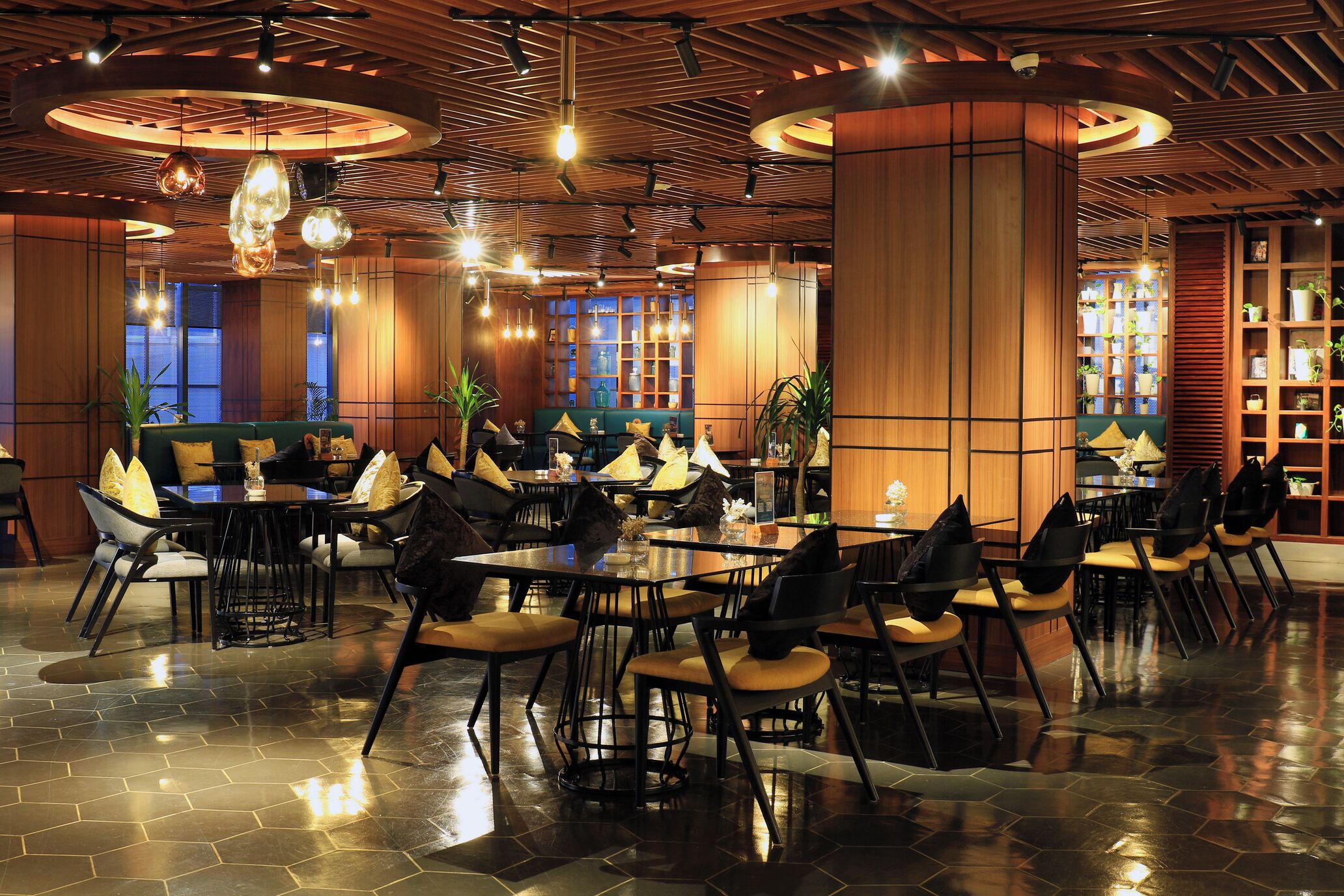 Een ruim restaurant met hoge plafonds, houten lambrisering en moderne verlichtingsarmaturen. Tafels en stoelen staan klaar voor de gasten.