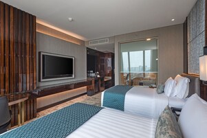 Ein modernes Hotelzimmer mit zwei Betten, einem Fernseher, einer Minibar und Blick auf die Stadt.