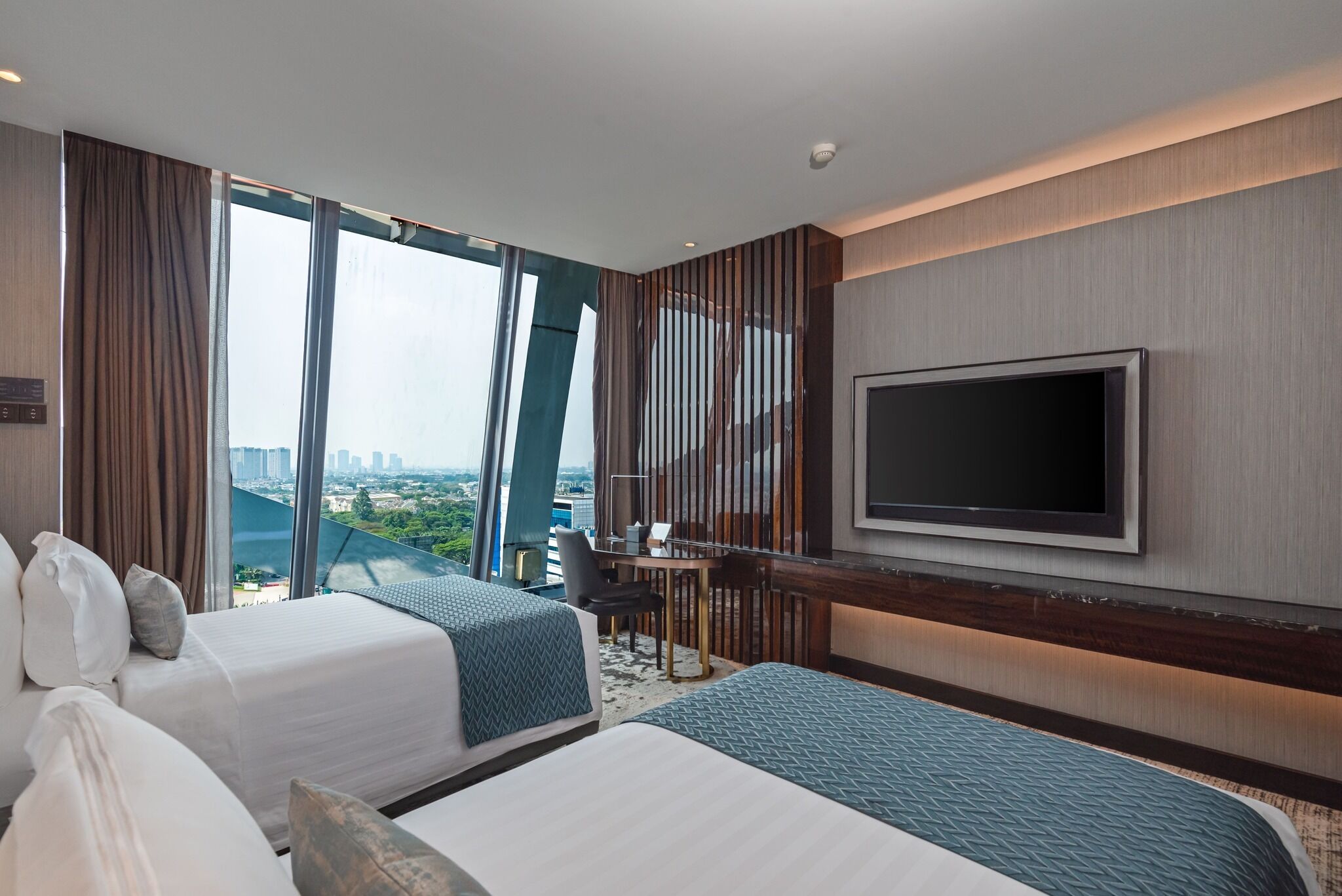 Habitación de hotel con dos camas, televisión, escritorio y vista a un paisaje urbano.