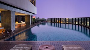 Una piscina infinita moderna con terraza de madera, sillones de descanso y balaustrada de cristal.