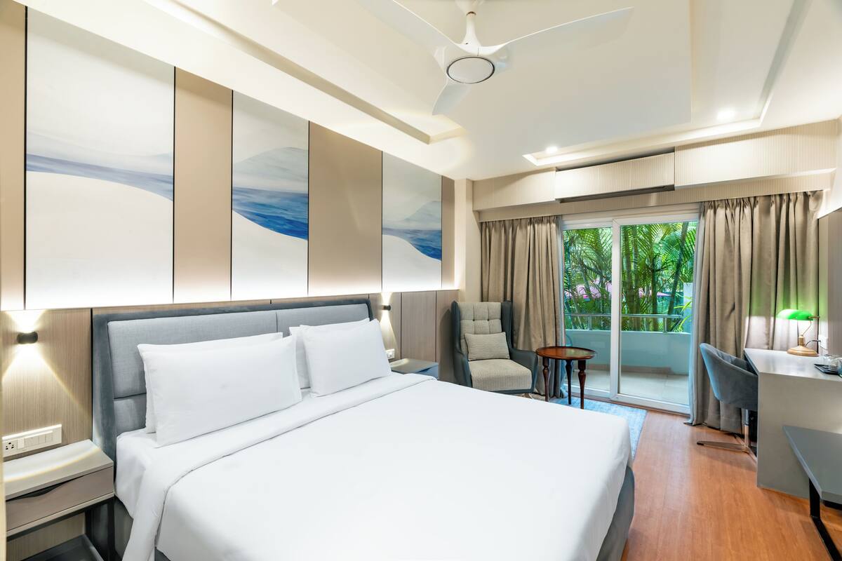 Habitación de hotel moderna con una cama grande, un escritorio, una silla y vistas a zonas verdes por la ventana.