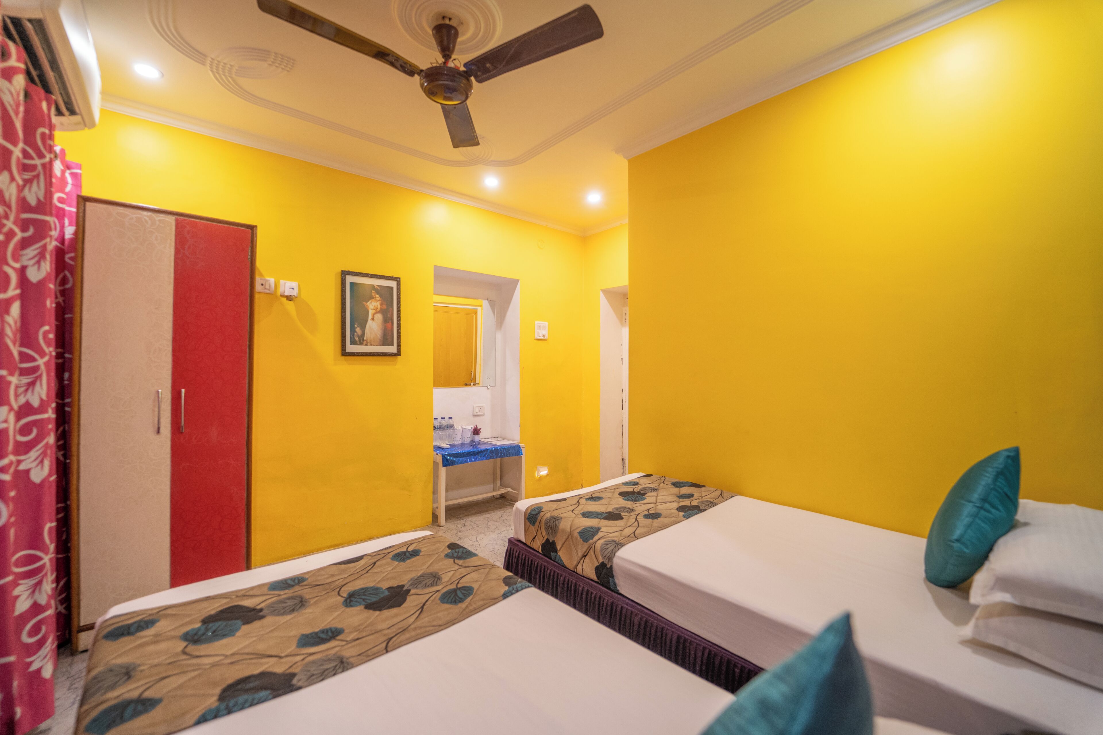 A room with two beds, a ceiling fan, a red door, and a bathroom visible through an open door.