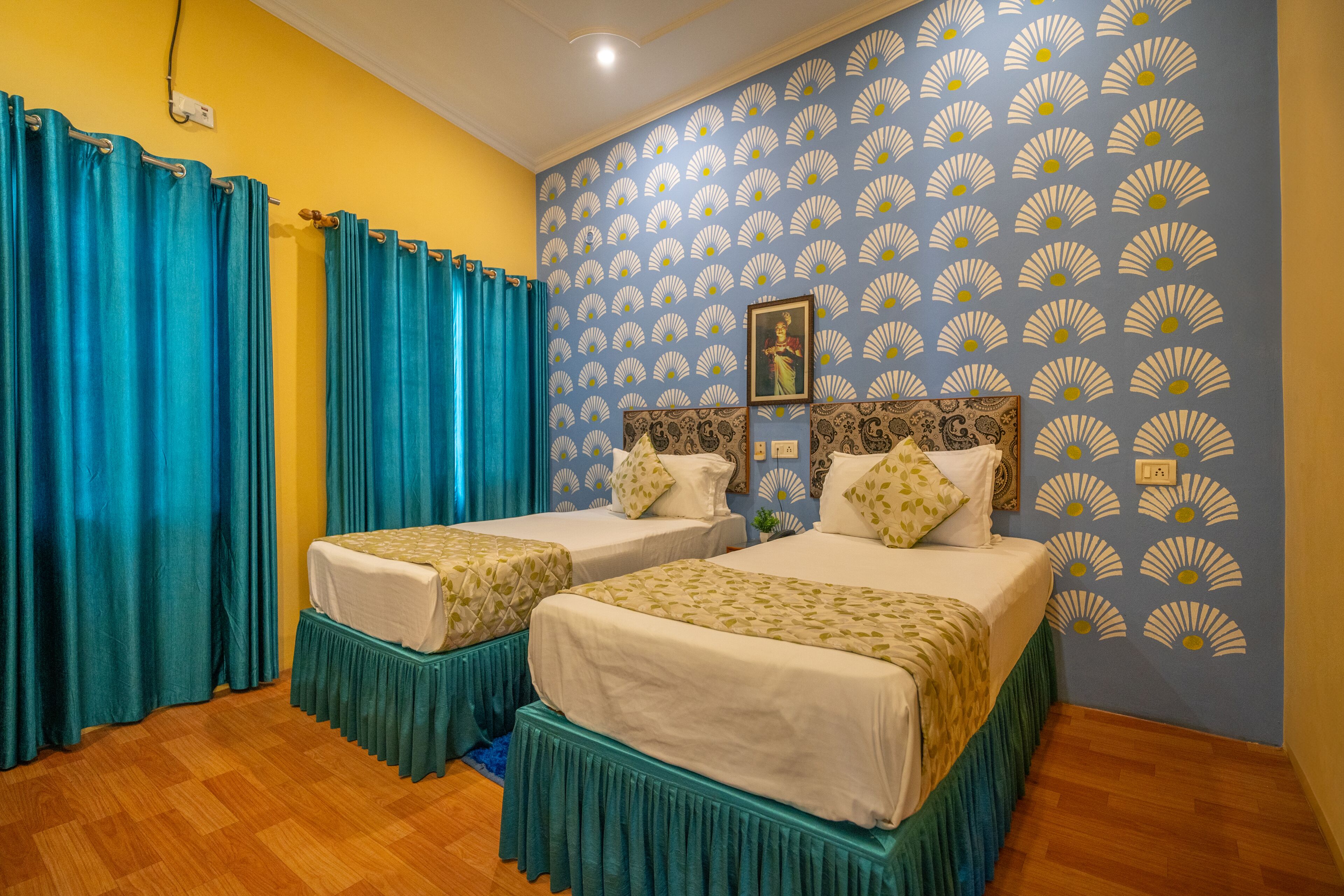Una habitación con dos camas, cortinas color turquesa, un papel tapiz estampado y suelo de madera.