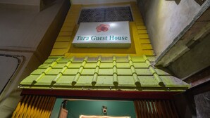 A sign for 'Tara Guest House' with a green and yellow facade, a tiled roof, and a small window with a decorative grill. - Tara Guest House (Varanasi)