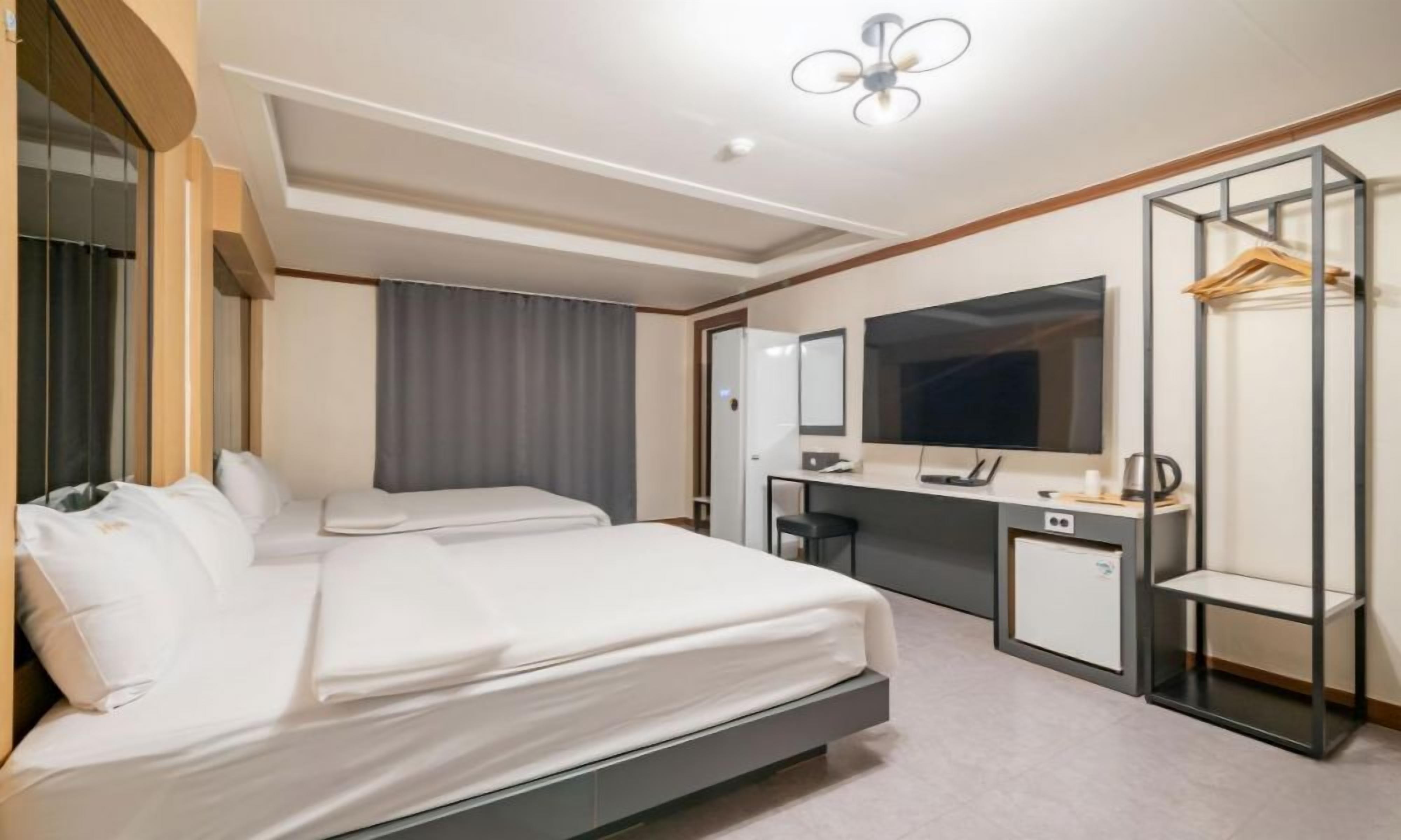A hotel room with two beds, a desk with a computer, a mirror, and a wardrobe.