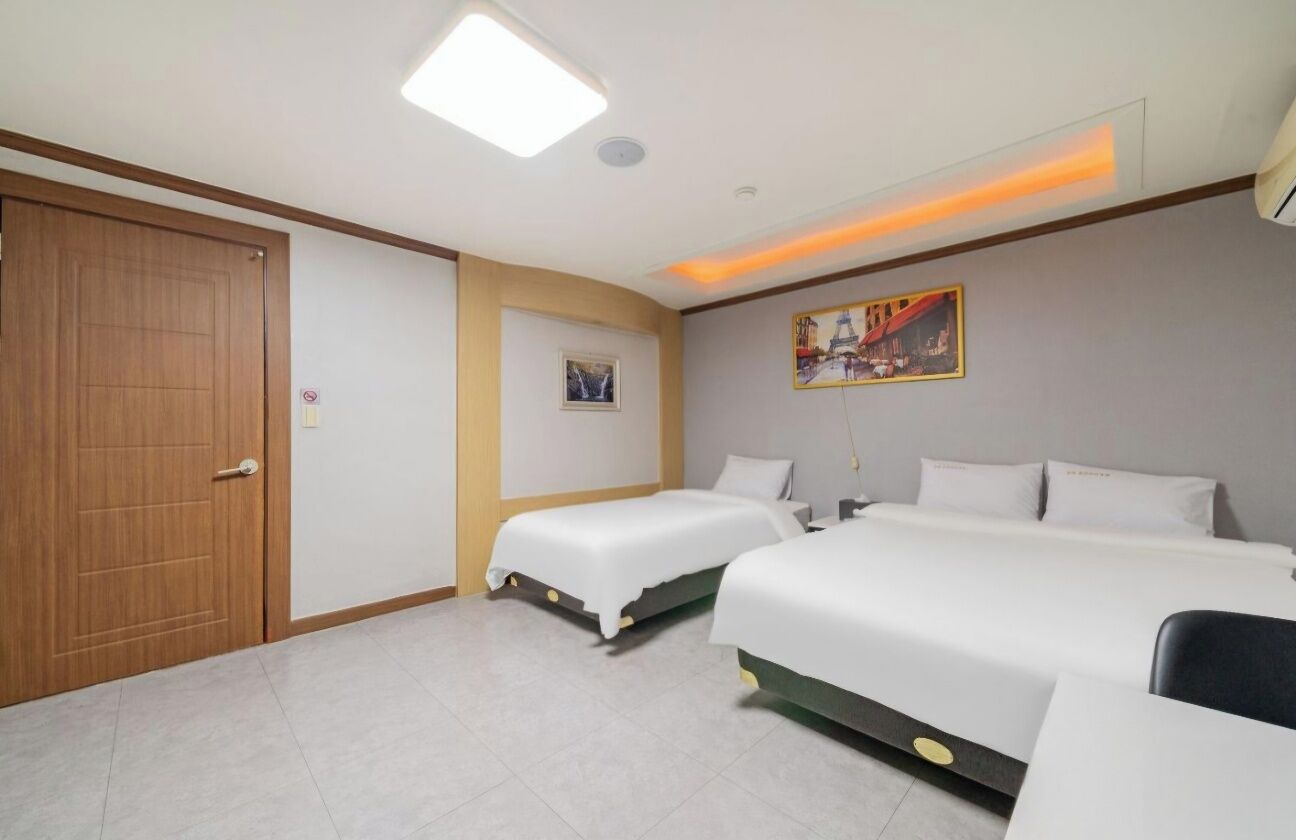 A hotel room with two single beds, a wooden door, a small framed picture, and a painting on the wall.