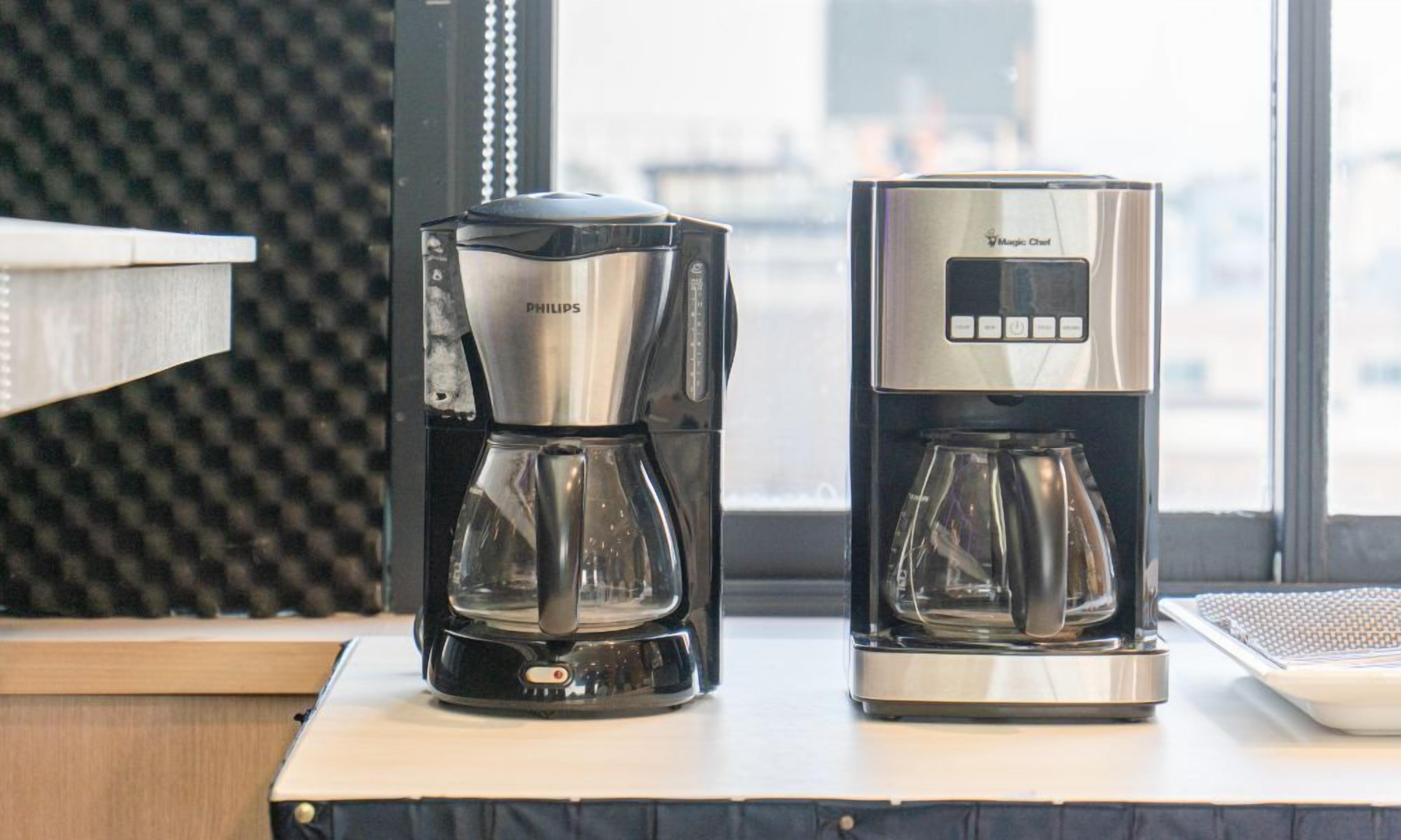 Due macchine da caffè, una PHILIPS e una Magic Chef, su un tavolo con una finestra sullo sfondo.