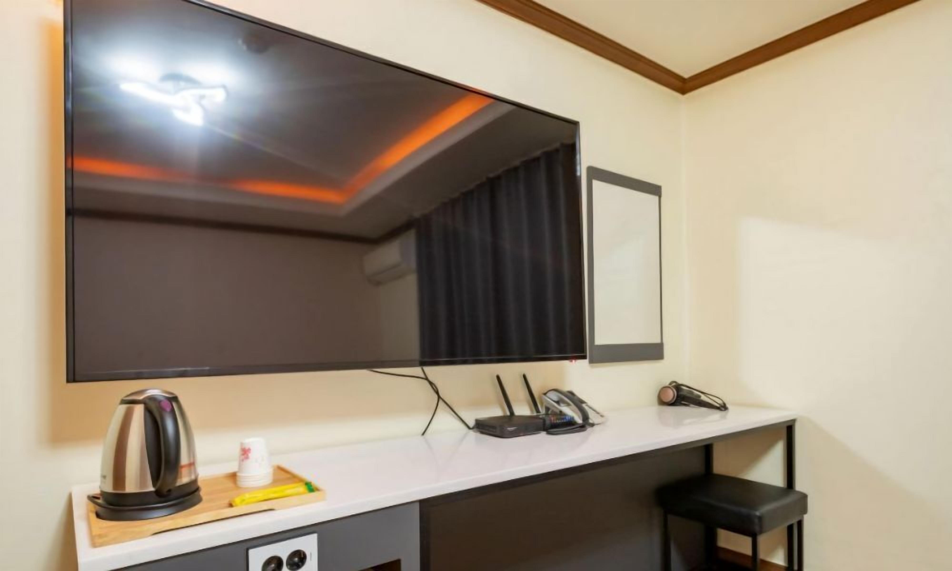 Habitación de hotel con un espejo grande, un escritorio con una tetera, un teléfono y un taburete pequeño.