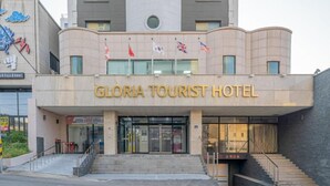 L’extérieur de l’hôtel Gloria, un établissement touristique au design moderne, se distingue par son entrée imposante avec des portes vitrées et un escalier menant à l’entrée.