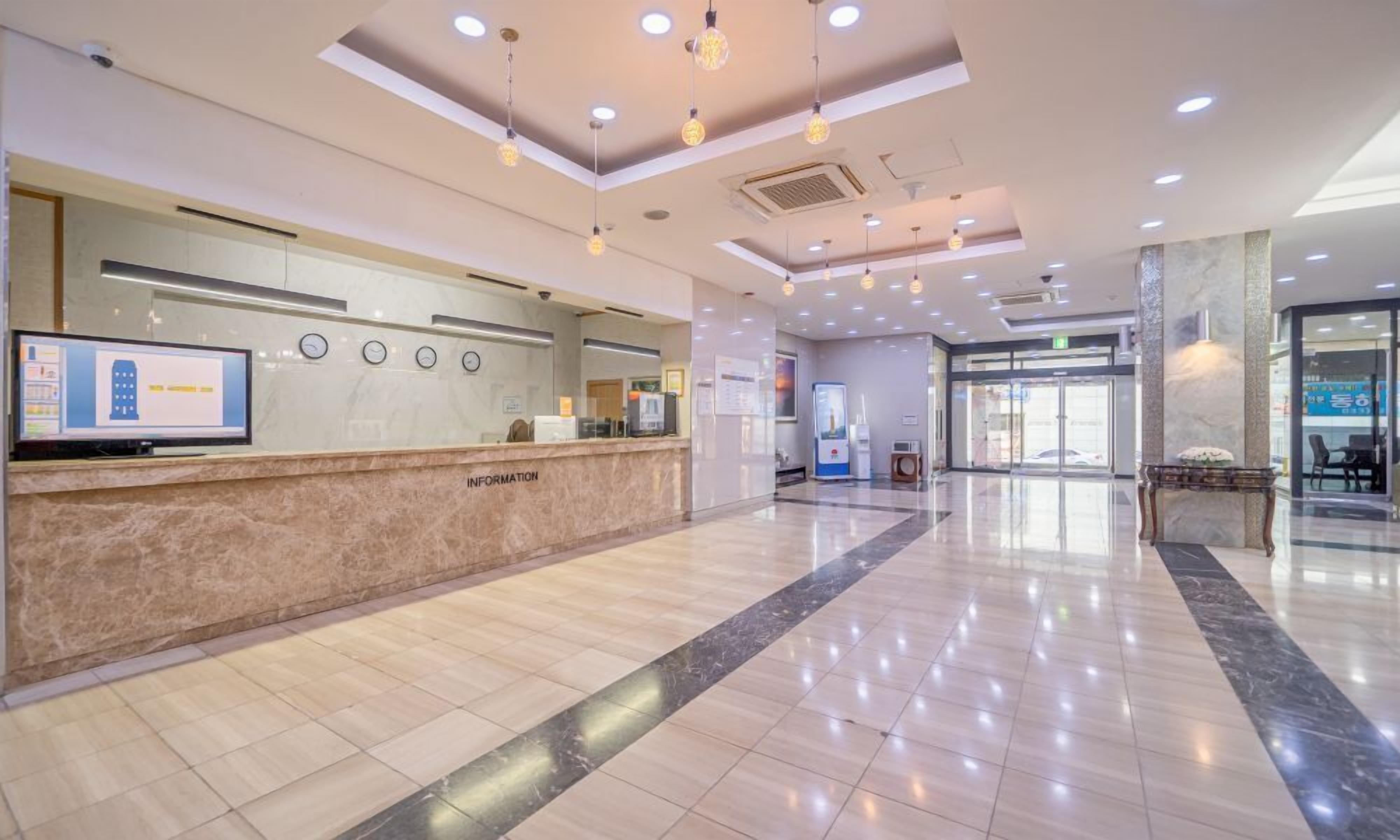 Et hotellets receptionområde med en marmordisk, et digitalt informationsskilt og et moderne loftdesign.