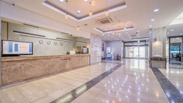 Et hotellets receptionområde med en marmordisk, et digitalt informationsskilt og et moderne loftdesign.