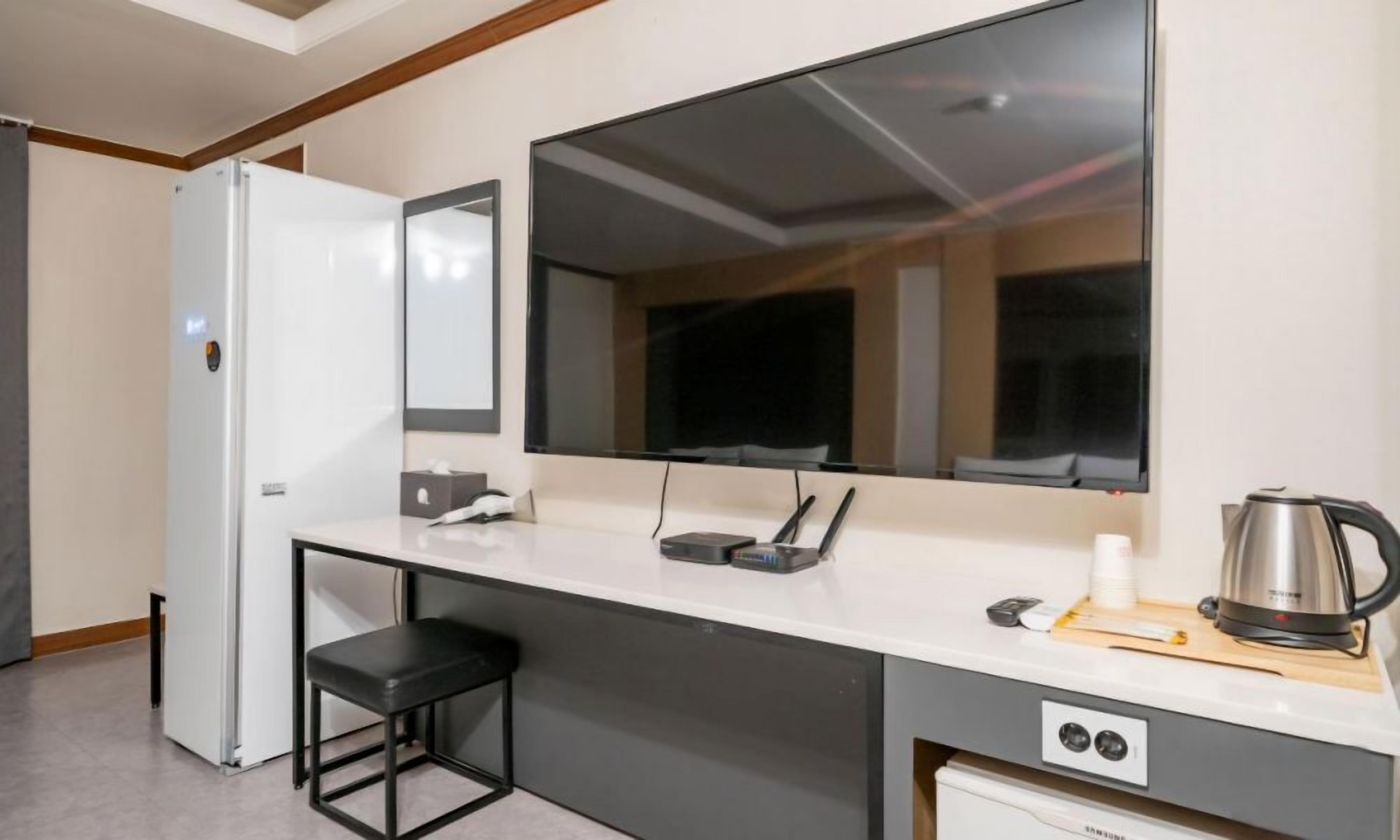 Una kitchenette compacta con cubierta blanca, un taburete negro, un hervidor de acero inoxidable y un microondas.