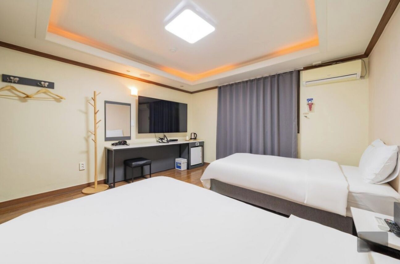 A hotel room with a bed, a desk with a chair, a mirror, a wardrobe, and a window with curtains.