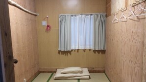 Una piccola stanza in legno con pavimento in tatami, un futon, una singola lampada a sospensione e una finestra con tende.