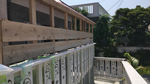 Un balcone in legno con ringhiera in metallo e vista su un edificio moderno e vegetazione sullo sfondo.