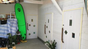 Una stanza con pavimento in legno, un surf tavola verde, una scala, un tavolo con una coperta e una pianta in vaso.