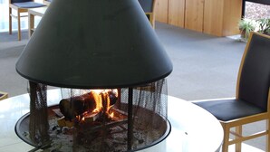 A round table with a black fire pit in the center, surrounded by wooden chairs with black cushions.