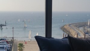 A view of the sea with sailboats, a rocky shoreline, and a paved walkway. - TLV Suites on the beach (Tel Aviv)