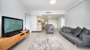 Una sala de estar moderna con una televisión de pantalla plana sobre un mueble de madera, un sofá gris y una alfombra gris.