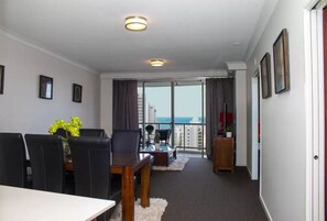 A modern living room with a dining area, a large window with a view of the city, and a balcony with a view of the sea. - GCA Chevron Renaissance (Surfers Paradise)