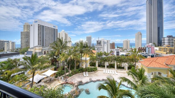 Un resort con piscina, palmeras y un horizonte urbano de fondo.