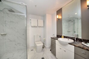 A modern bathroom with a glass shower enclosure, a white toilet, a vanity with a large mirror, and marble flooring. - GCA Chevron Renaissance (Surfers Paradise)