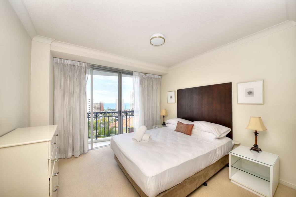 A hotel room with a large bed, a desk, a nightstand, and a view of the city through the window.
