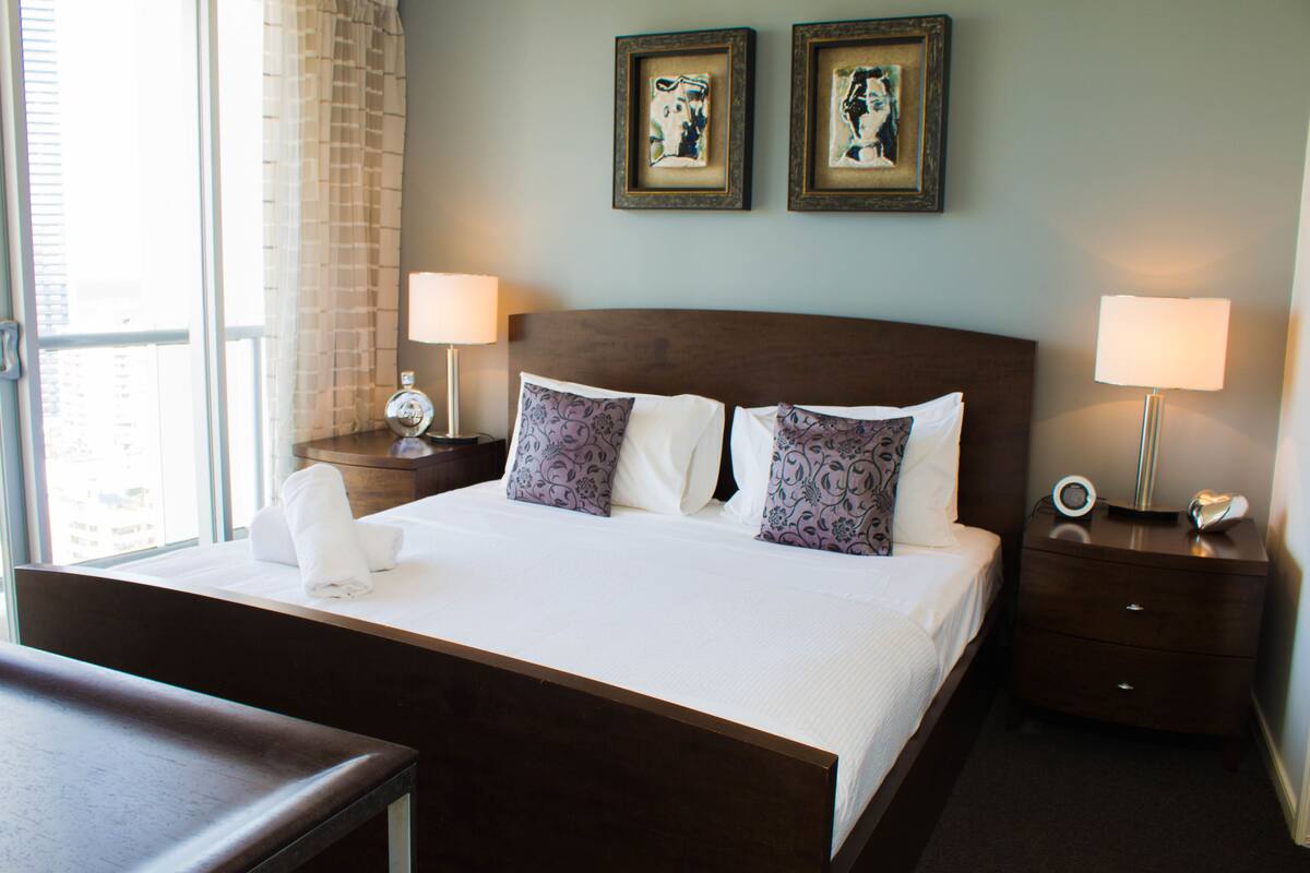 A hotel room with a large bed, two bedside tables with lamps, a nightstand, and two framed pictures on the wall.