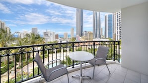 Un balcón con mesa y sillas, con vistas a un paisaje urbano con edificios altos y palmeras.