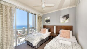 Habitación de hotel con dos camas, un ventanal amplio con vista a la ciudad, un ventilador de techo y obras de arte en la pared.
