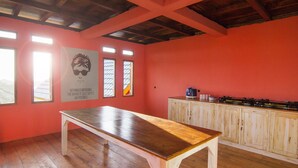 A room with a wooden table, a kitchen area with cabinets, and a ceiling with exposed beams. - One Tree Hill - Hostel (Labuan Bajo)