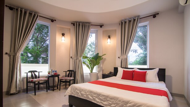 Una habitación de hotel con una cama grande, dos sillas, una mesita pequeña y una planta en maceta.