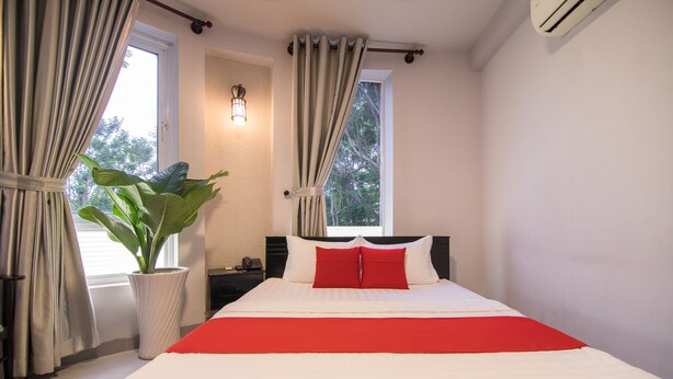 A neatly made bed with a red accent, a potted plant, and a nightstand with a lamp. - Bin Bin Hotel 1 - Near RMIT University (Ho Chi Minh City)