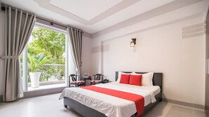 Habitación de hotel con una cama grande, una ventana con cortinas, una mesita con una silla y una planta en maceta.