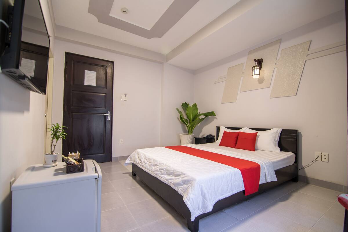 Ein modernes Schlafzimmer mit einem Bett, einem kleinen Schreibtisch, einem Blumentopf und einer Tür.