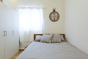 A bedroom with a bed, pillows, a clock, and a window with curtains.