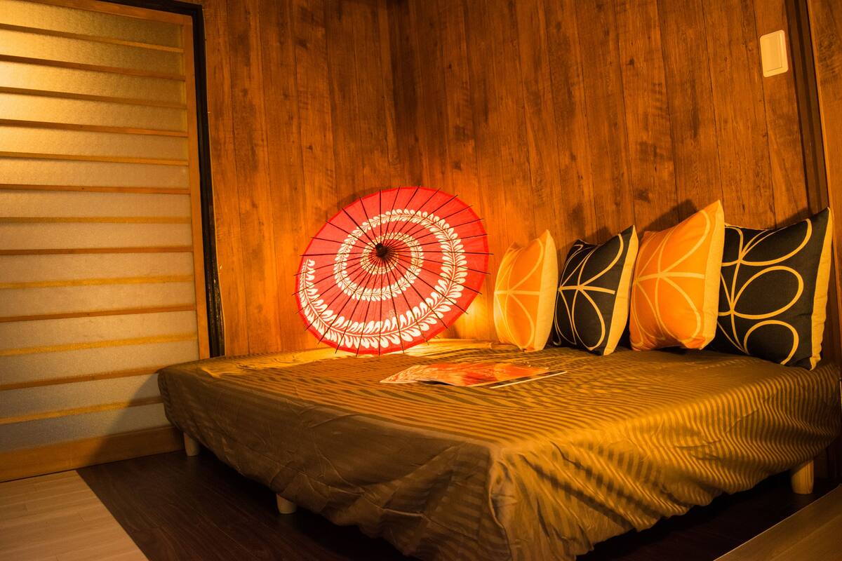 A bed with a patterned bedspread, a red umbrella decoration, and geometric pillows.