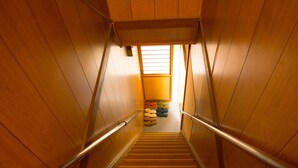 A wooden staircase with metal handrails leading to a landing where colorful bags are stacked. - Oyado Toji 3 (Kyoto)